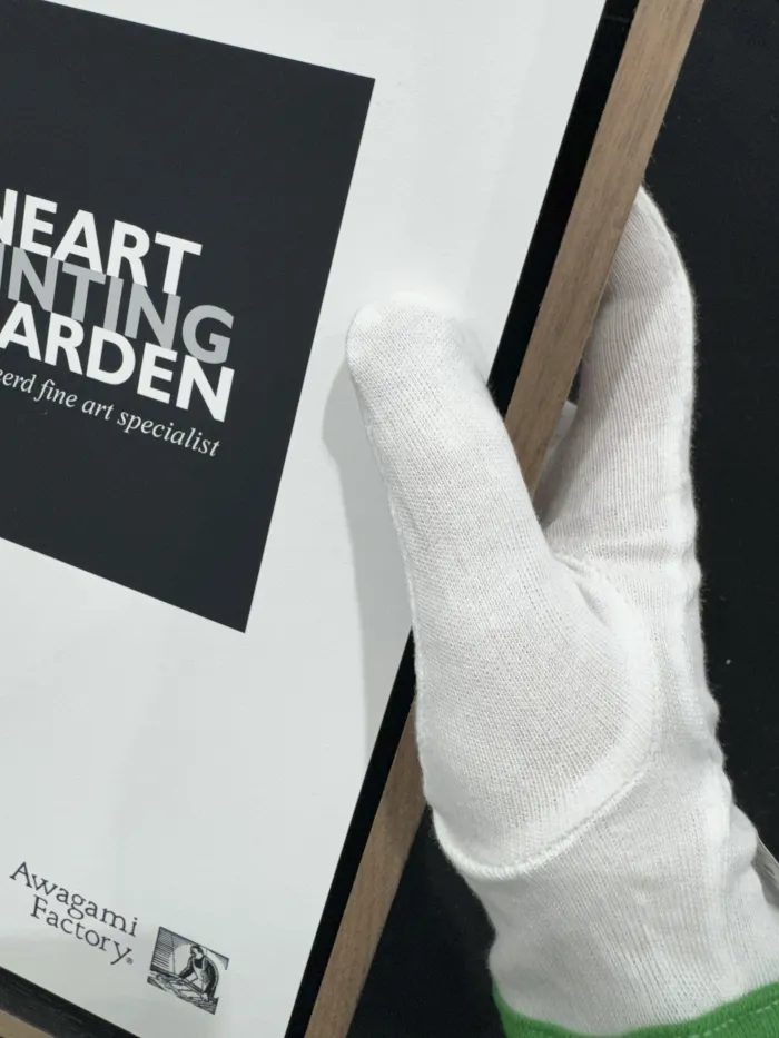 Hand met witte katoenen handschoen houdt een ingelijste fine art print vast.